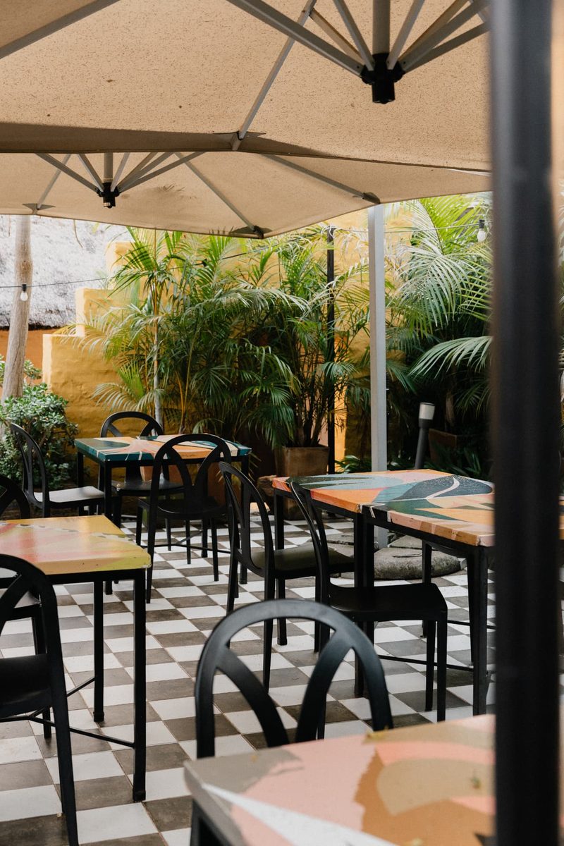 Hand-painted Courtyard tables and black chairs framed by palms and festoon lights