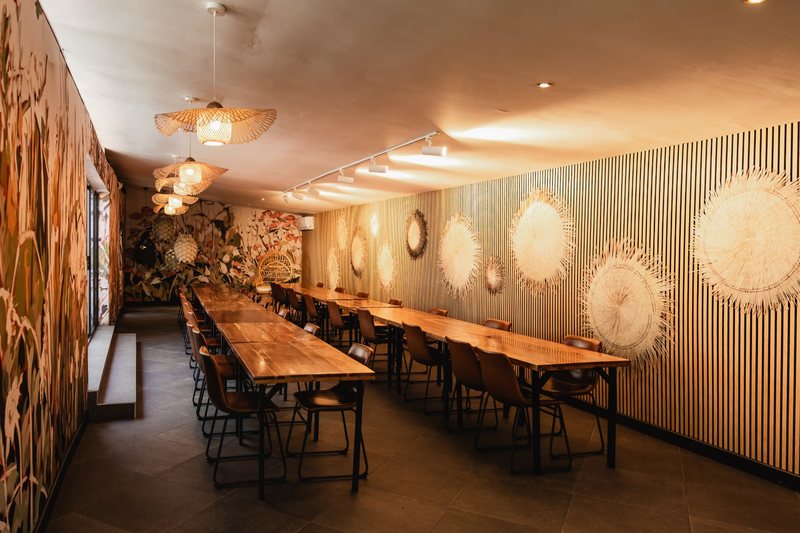 Bloot seen end-on, its two long tables running towards the mural under warm track lighting