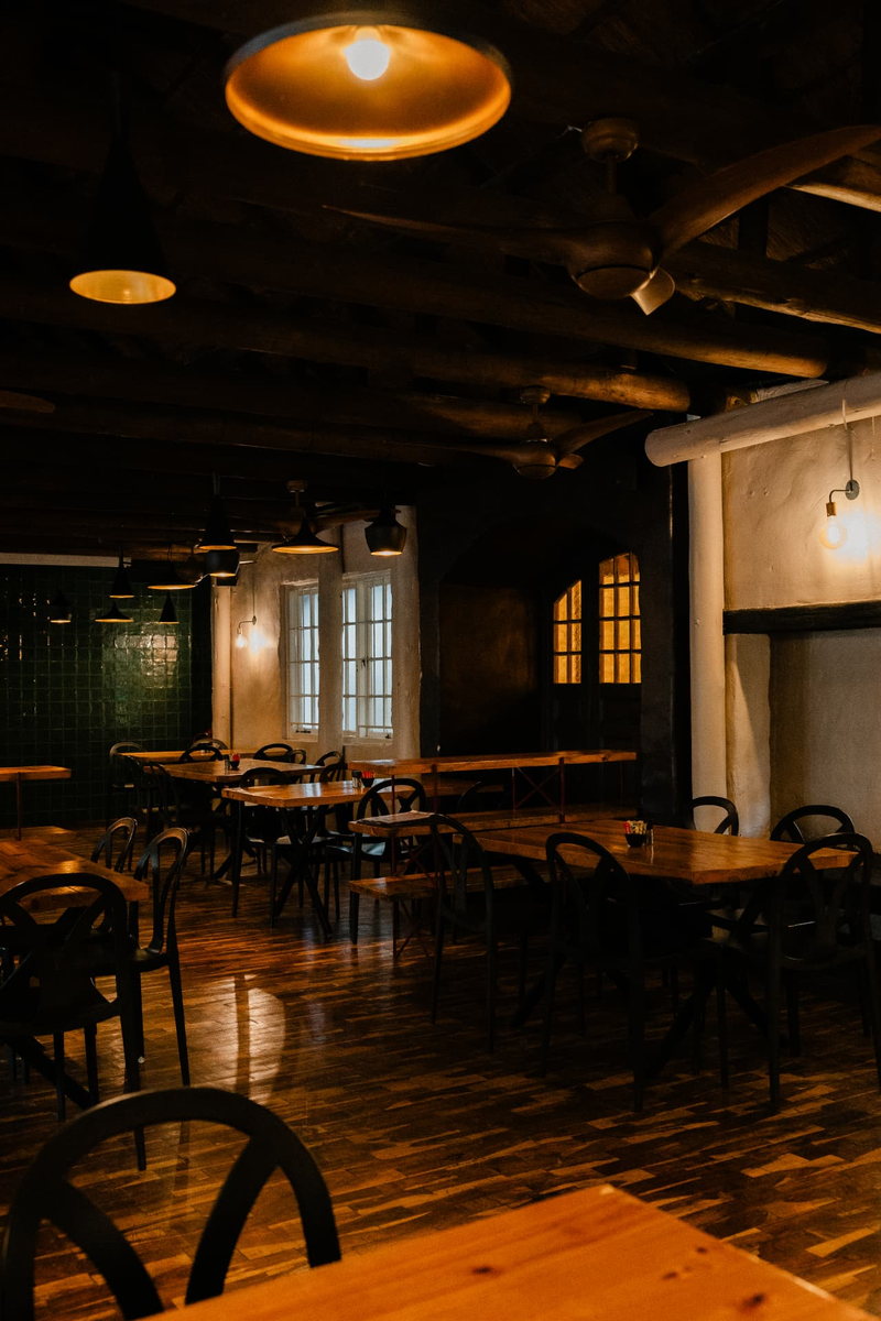 The full-height view of the Main Function Room at night, pendant lights over timber tables leading to the glowing arched doorway