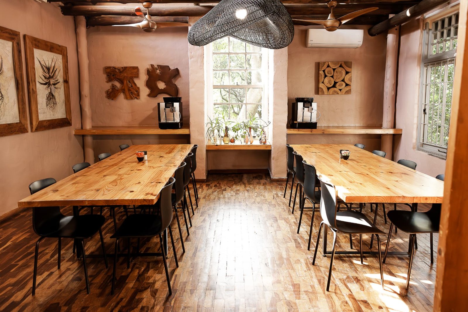 The Oak Room at Blos Café with two long pine tables and black chairs beneath a woven pendant light and thatched beams