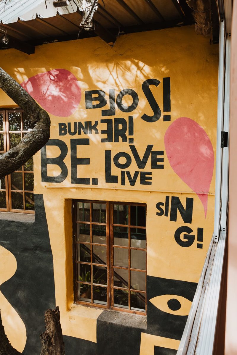 The hand-painted yellow Blos Bunker mural reading 'Blos! Bunker! Be. Love. Live. Sing!' beside the terrace windows