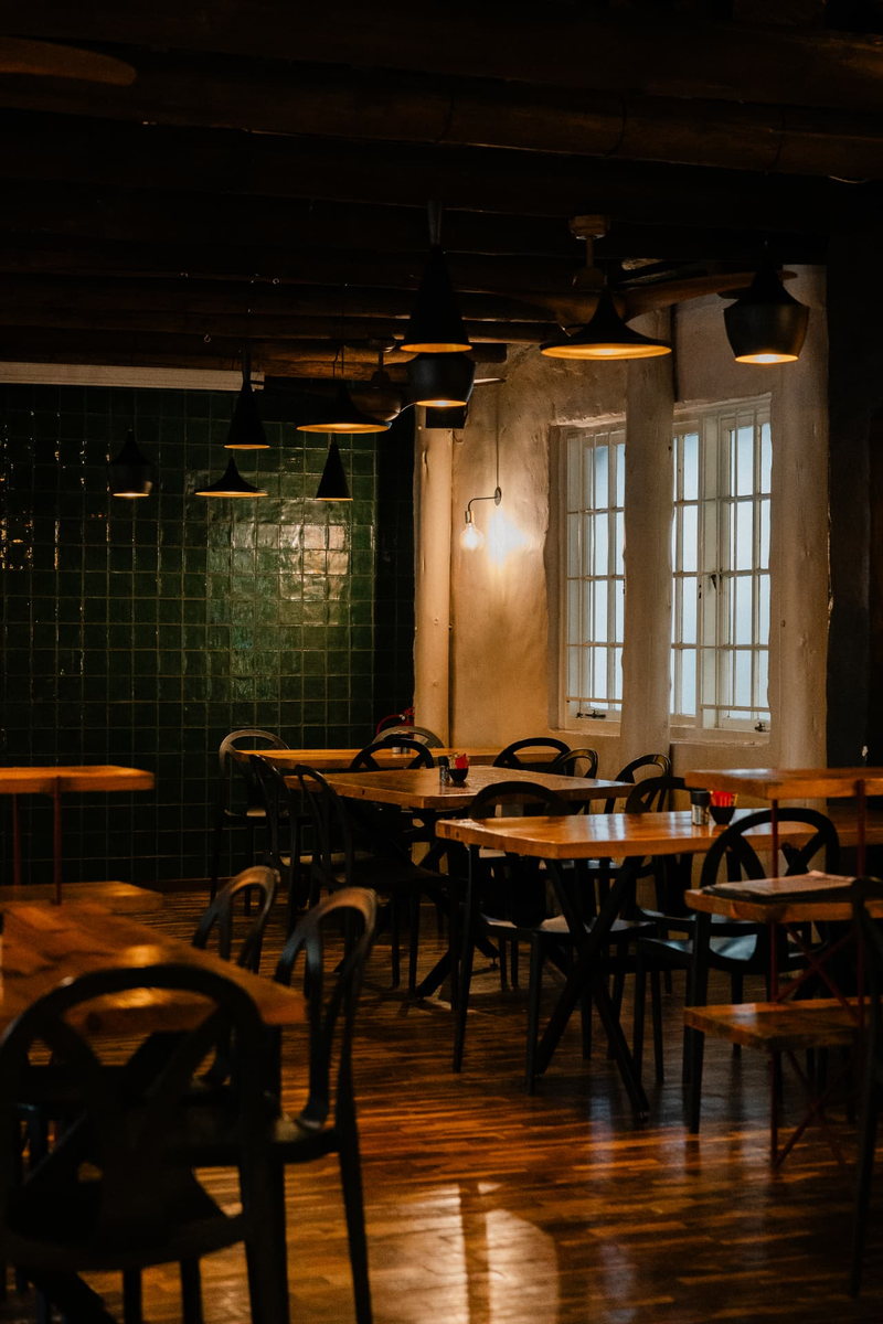 Timber tables and black bentwood chairs beside the Main Function Room's dark green tiled wall and tall paned window