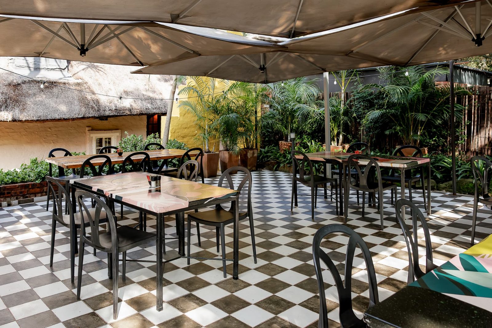 The Courtyard at Blos Café with tables under cream umbrellas on a black-and-white chequerboard floor
