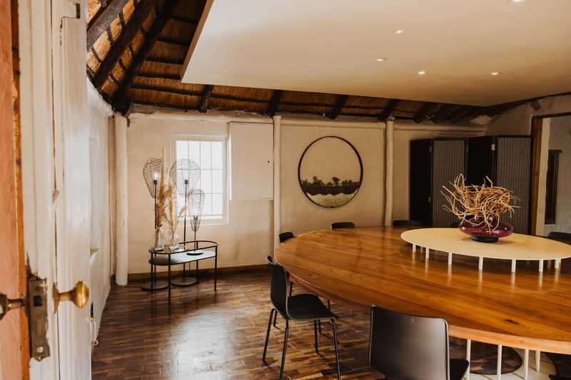 Looking into the Cinema Room through an open timber door: the curved walnut table, wire pendant sculptures on a side console and a circular landscape artwork on the whitewashed wall