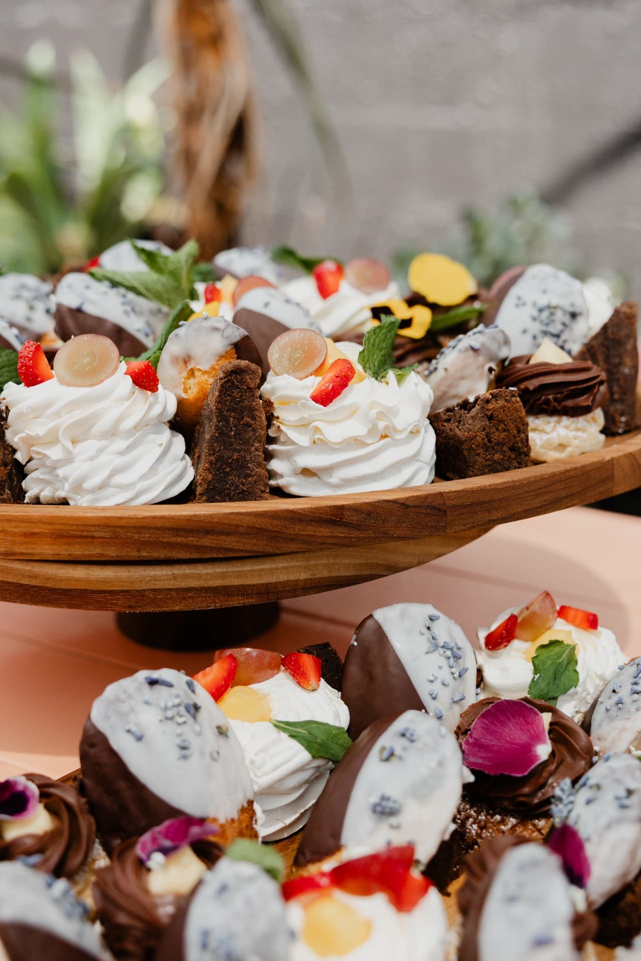 Tiered dessert platters at Blos: mini pavlovas with strawberries and grapes, chocolate-dipped meringues with lavender, brownies and chocolate-piped tartlets on a wooden cake stand