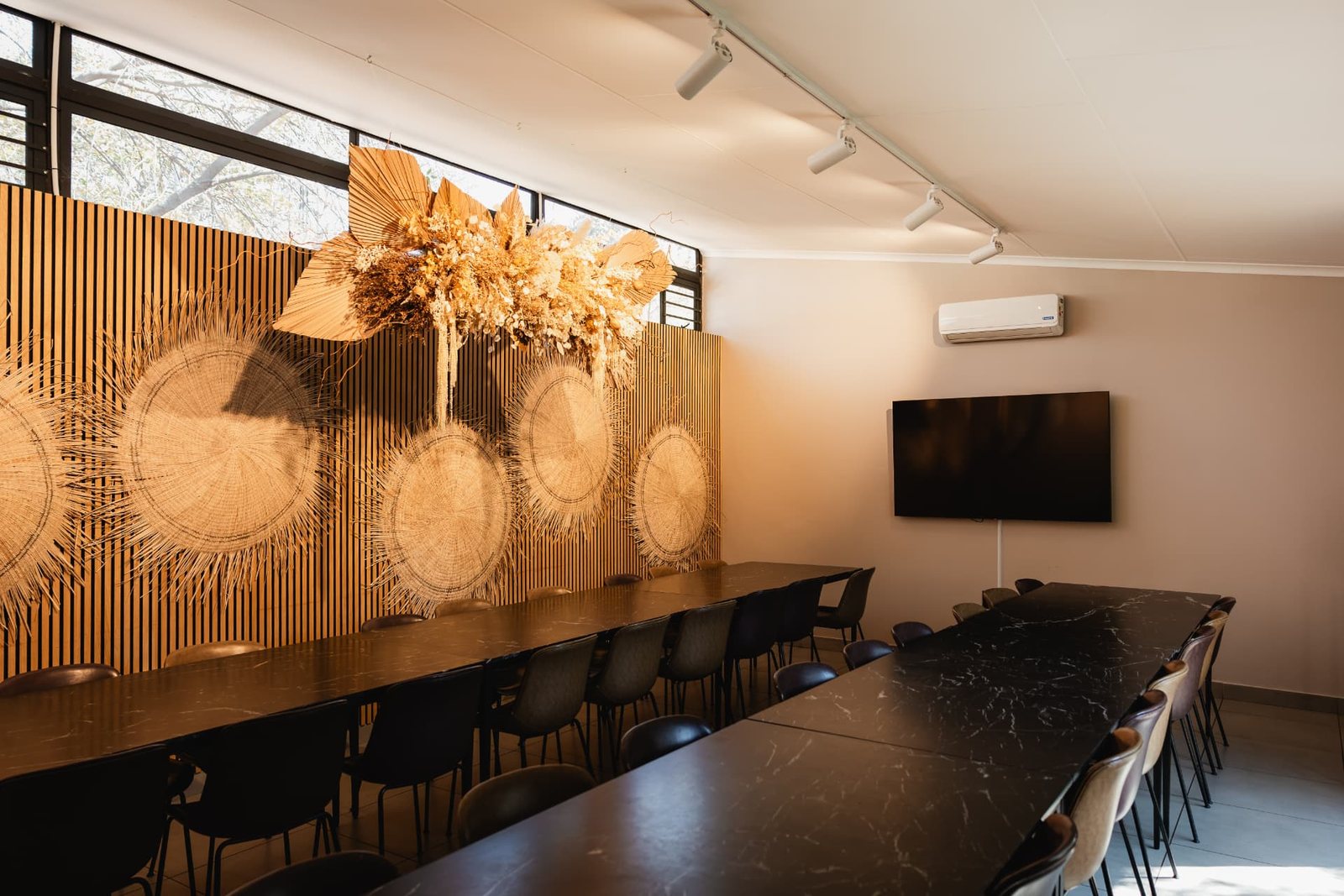 Still at Blos Café with long black marble tables and dark chairs facing a slatted timber wall hung with woven discs and a dried floral installation