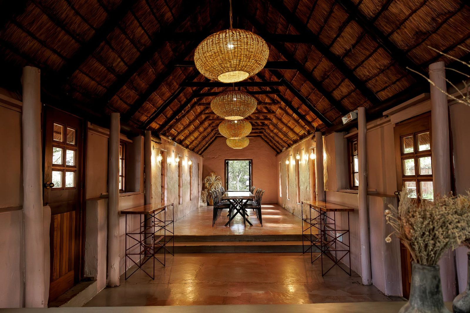 Inside the Chapel at Blos Café, looking down the aisle to a long table beneath woven pendant lights and a thatched roof