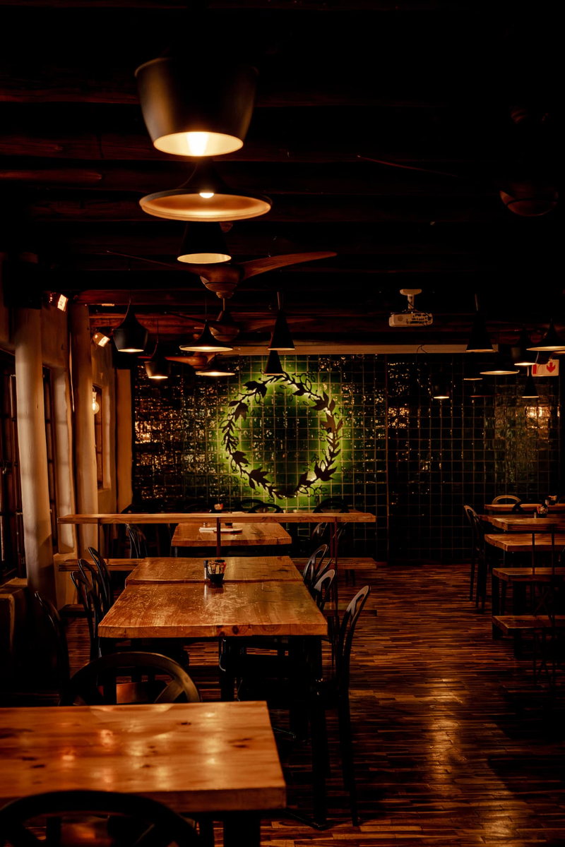 Long timber tables under low pendant lighting in the Main Function Room, with a leafy wreath motif on the green tiled wall beyond