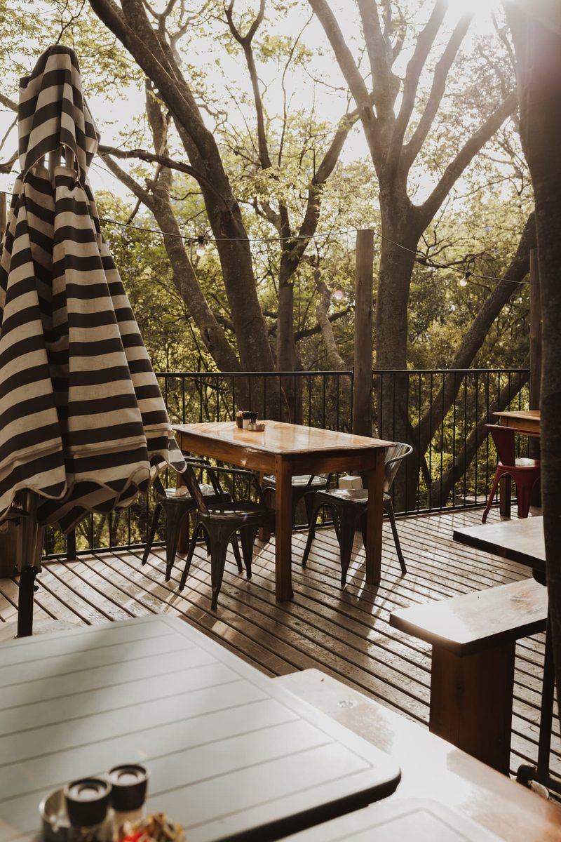 A timber table and metal chairs on the raised terrace deck, with festoon lights strung between the trees